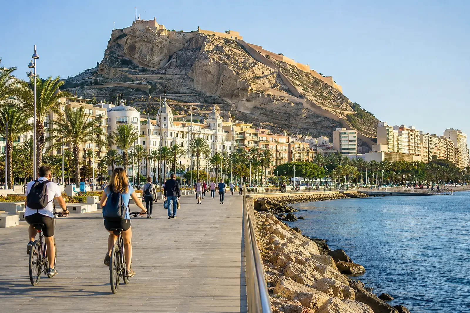 Cyklande människor på strandpromenaden i Alicante under soligt väder